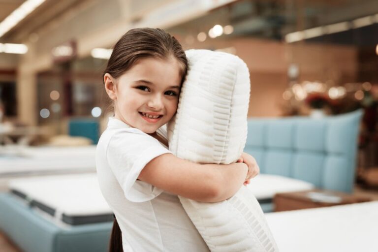 Nice little girl hugs pillow in store of orthopedic mattresses. Testing softness of pillow
